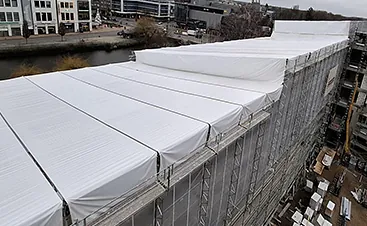 Großflächiges weißes Wetterschutzdach über einem eingerüsteten Gebäude zum Schutz vor Regen und Witterung bei Bau- und Sanierungsarbeiten.