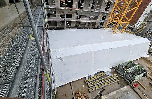 Weiße Schutzeinhausung auf einer Baustelle am Schlicksweg 2 in Hamburg mit angrenzendem Fassadengerüst und Baukran für geschützte Bauarbeiten.