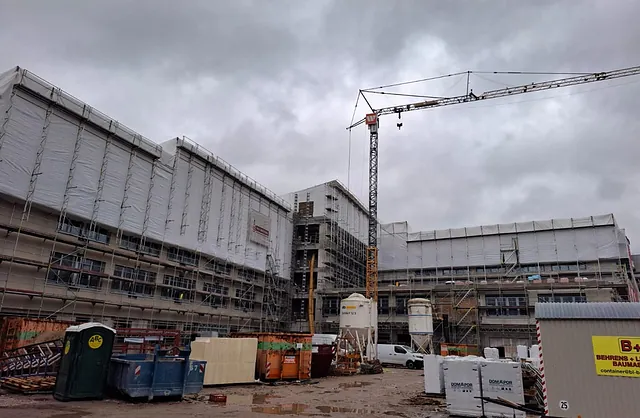 Großbaustelle der Sparkasse Neumünster mit eingerüsteten Gebäudefassaden, weißer Wetterschutzverkleidung und Baukran im Innenhof.