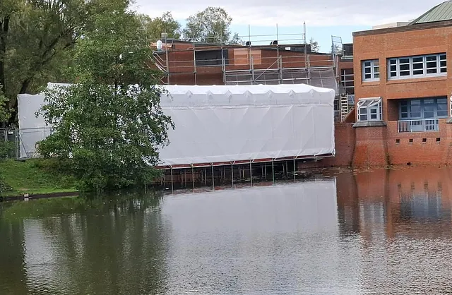 Weiße Schutzeinhausung an einer Fußgängerbrücke über dem Wasser in Hamburg-Wilhelmsburg für wettergeschützte Brückensanierungsarbeiten.