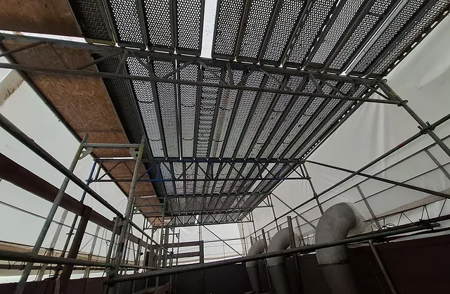 Innenansicht eines Industriegerüsts mit Gitterrost-Arbeitsplattformen und weißer Schutzfolie rund um Rohrleitungen im Klärwerk Dradenau in Hamburg.