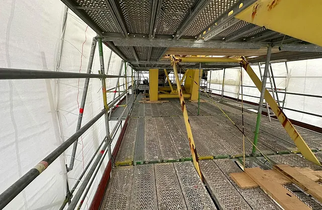 Innenansicht eines eingehausten Industriegerüsts mit begehbaren Gitterrostbelägen und Stahlkonstruktion für Wartungs- und Sanierungsarbeiten.