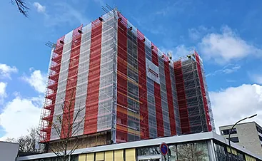 Mehrstöckiges Gebäude mit Fassadengerüst und rot-weißen Schutznetzen für sichere Fassadenarbeiten und Gebäudesanierungen im Raum Hamburg.